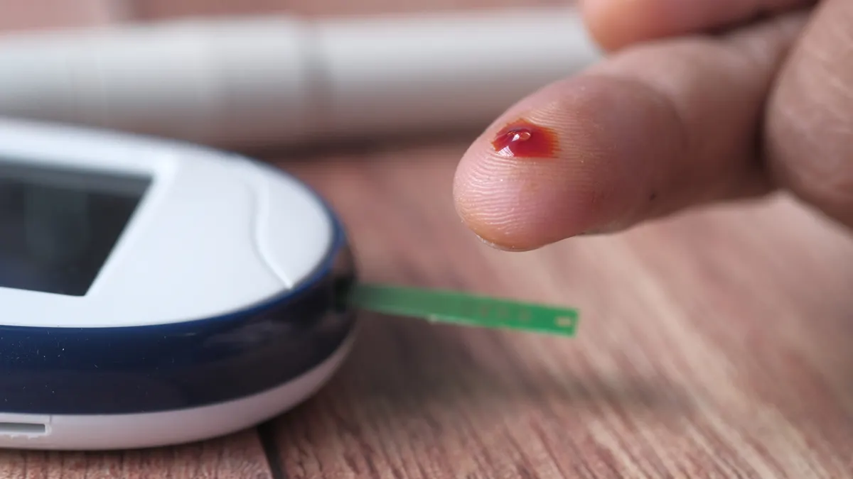 finger prick blood test beside a glucose meter