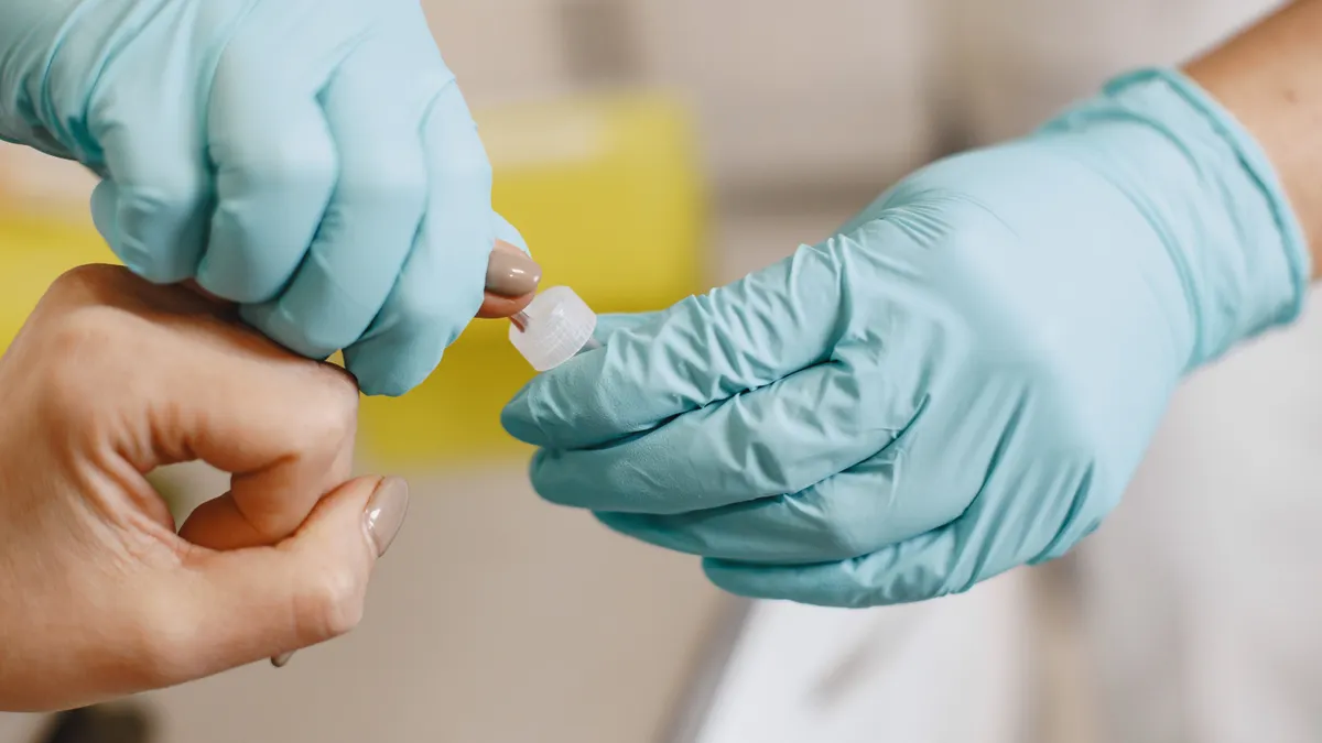 Gloved hands doing a finger prick blood test