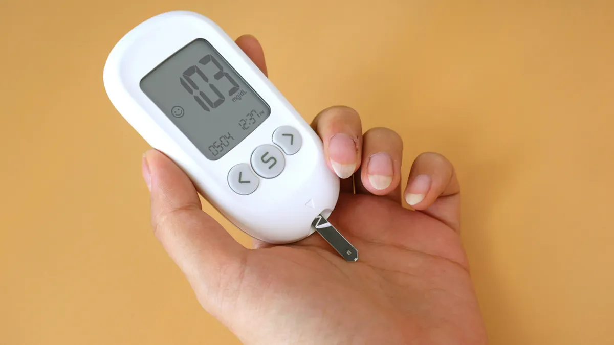 What to Do If Your Blood Sugar Is Too High During Pregnancy — A person holding a digital blood sugar meter